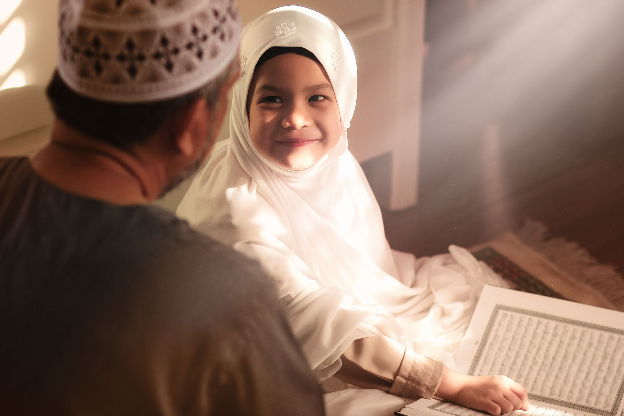 Religious Asian Muslim Man teaching his 6 years old daughter to learn the Quran and study Islam after pray to God at home .Sunset light shining through the window.Peaceful and Marvelous warm climate.