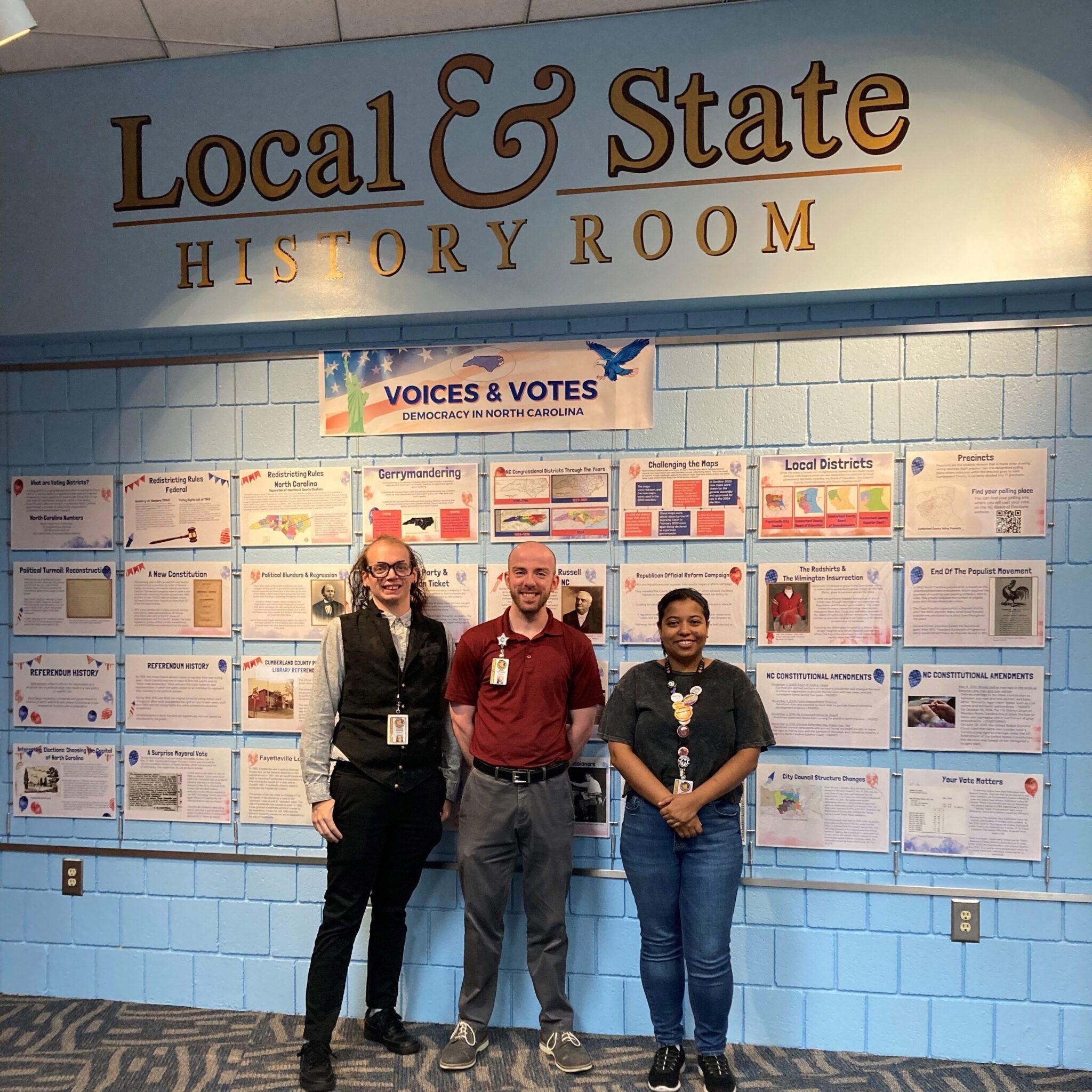 Three people stand in front of wall that reads "Local and State History Room"