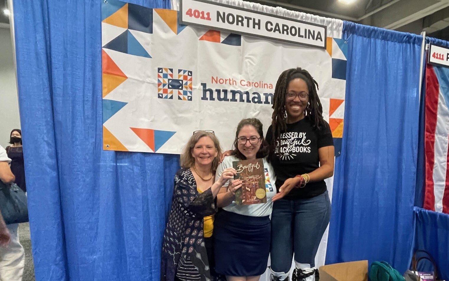 Three women hold a book and smile